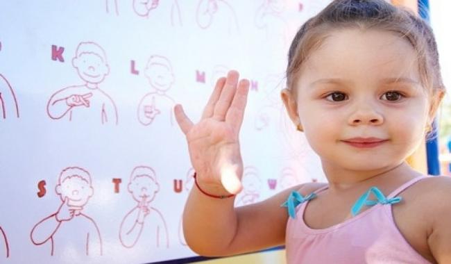 little girl in pink tank top in front of a white board showing sign language