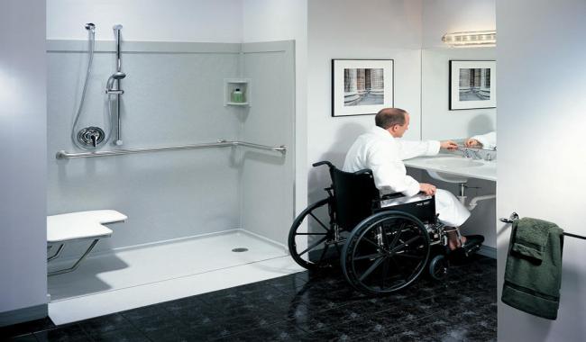 An image of a man in a wheel, washing his hands in accessible sink, next to accessible shower