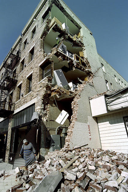 Woman standing in front of earthquake-damaged apartment building