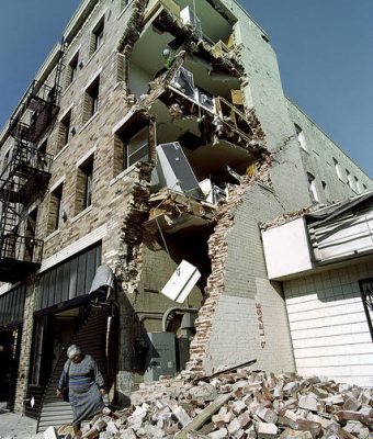 Woman standing in front of earthquake-damaged apartment building